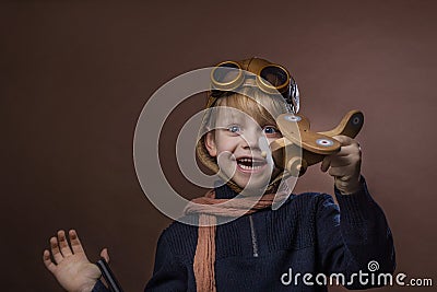 Happy child dressed in pilot hat and glasses. Kid playing with wooden toy airplane. Dream and freedom concept. Retro toned Stock Photo