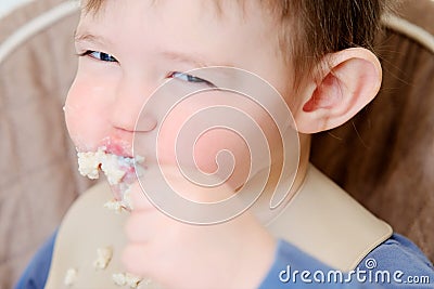 A happy child eats porridge with a spoon while sitting on a high chair. B Stock Photo