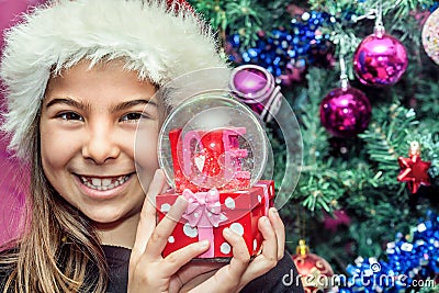 Happy child girl in a Christmas hat holding glass globe gift of Stock Photo