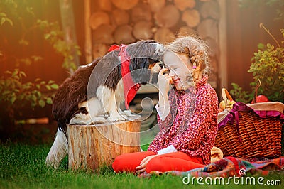 Happy child girl having fun playing with her dog in sunny autumn garden Stock Photo