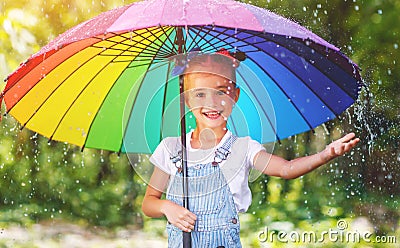 Happy child girl laughs and plays under summer rain with an umbrella. Stock Photo