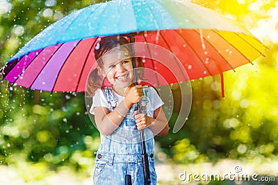 Happy child girl laughs and plays under summer rain with an umbrella. Stock Photo