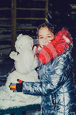 Happy child girl plaing with a snowman on a snowy winter walk.A teenage girl sculpts a snowman Stock Photo