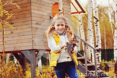 Happy child girl playing little gardener in autumn and picking leaves into basket Stock Photo