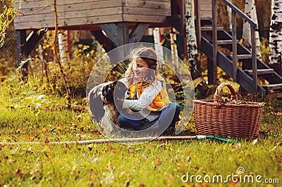 Happy child girl playing little gardener in autumn and picking leaves into basket. Seasonal garden work. Stock Photo