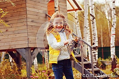 Happy child girl playing little gardener in autumn and picking leaves into basket. Seasonal garden work. Stock Photo