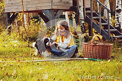 Happy child girl playing little gardener in autumn and picking leaves into basket. Seasonal garden work. Stock Photo