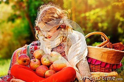 Happy child girl sitting with apples in autumn sunny garden Stock Photo