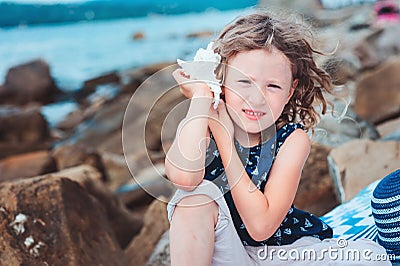 Happy child girl in stripe hat playing on the beach and listen to sea shell Stock Photo