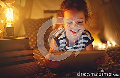 Happy child girl with tablet pc laughing in dark in tent at home Stock Photo