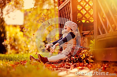 Happy child girl throwing leaves on the walk in sunny autumn garden Stock Photo