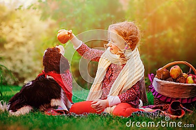 Happy child girl training her dog and giving him apple in sunny autumn garden Stock Photo