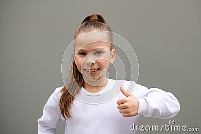 happy child girl in white sweatshirt show gesture by hand on grey scale wall background. Like gest Stock Photo