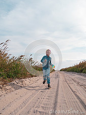 Happy child running jumping having fun on empty autumn beach. Blond girl walking on white sand road Stock Photo