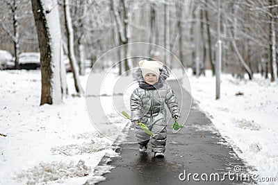 A funny girl in a warm silver jumpsuit runs along the path in winter Stock Photo