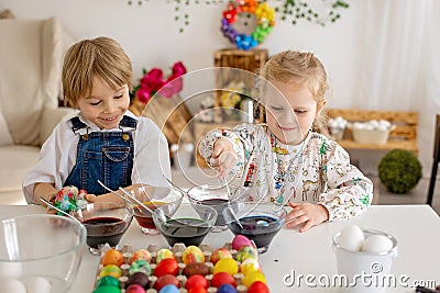 Happy childen, siblings, coloring eggs for Easter at home, sunny room Stock Photo