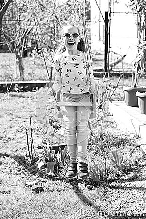 Happy childhood concept. Little child smile on swing in summer yard. Fashion girl in sunglasses enjoy swinging on sunny Stock Photo