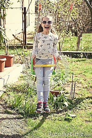 Happy childhood concept. Little child smile on swing in summer yard. Fashion girl in sunglasses enjoy swinging on sunny Stock Photo