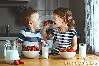 Happy children brother and sister eating strawberries with milk Stock Photo