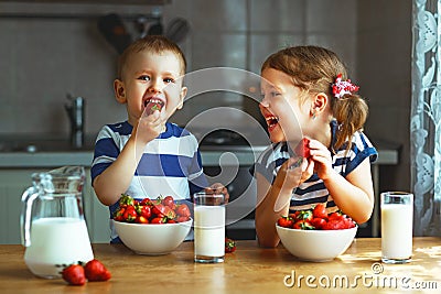 Happy children brother and sister eating strawberries with milk Stock Photo