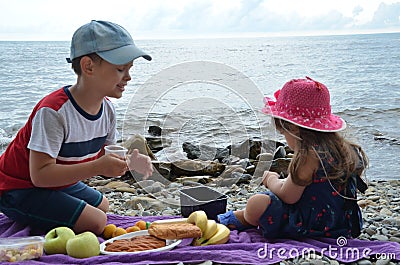 happy children brother and sister sit by the sea, have a picnic, eat fruit, pastries, drink juice and cocktail. Friends Stock Photo