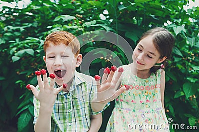 Happy children eating raspberry from fingers in summer garden Stock Photo