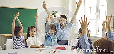 Happy school teacher and little children raising hands up and having fun in class Stock Photo