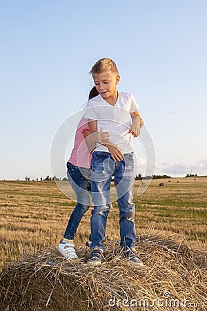 happy children jostling on haystack at sunset. kids, girl with boy standing in field Stock Photo