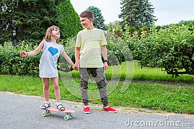 Happy children ride a skateboard in the park. The girl is riding on board Stock Photo