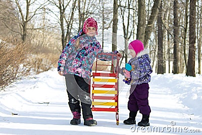 Happy children standing together on a walkway in a snowy winter park an holding the sleds Stock Photo