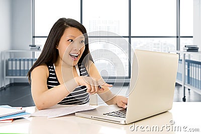 Happy chinese asian woman working and studying on her computer sitting at modern office desk smiling cheerful Stock Photo
