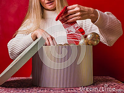 Happy Christmas. Preparing Christmas presents. Woman puts red socks with patterns in a large striped gift box Stock Photo