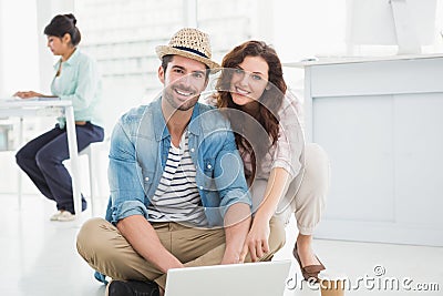 Happy colleagues sitting on the floor using laptop Stock Photo