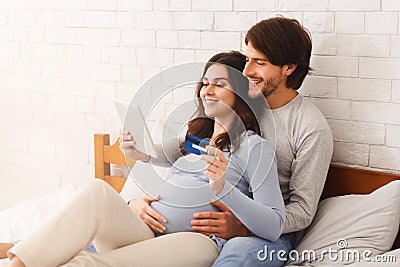 Happy couple awaiting baby and making online shopping on bed at home Stock Photo