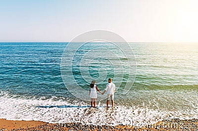 Happy couple on the beach with their backs to the camera. Honeymoon trip. The couple are traveling. Man and woman on the beach. Stock Photo