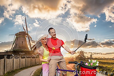 Happy couple on bike against traditional Dutch windmills in Zaanse Schans, Amsterdam area, Holland Editorial Stock Photo