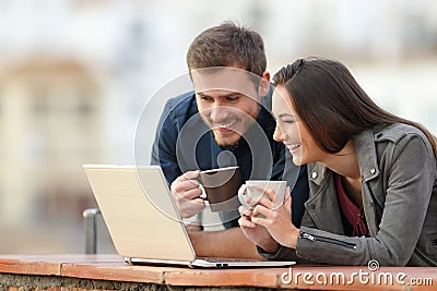 Happy couple checking laptop content on a balcony Stock Photo