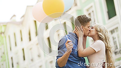 Happy couple with colorful air balloons kissing in street, tender relationship Stock Photo