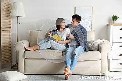 Happy couple covered with warm dark blue plaid reading book on sofa at home Stock Photo