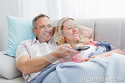 Happy couple cuddling on the couch watching television Stock Photo