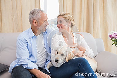 Happy couple cuddling with puppy on sofa Stock Photo