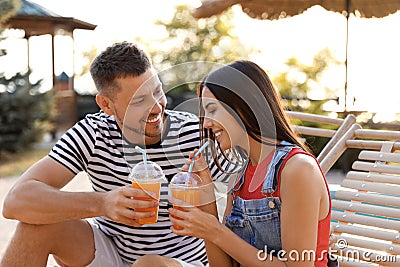 Happy couple with cups of refreshing drink resting in deck chairs outdoors Stock Photo