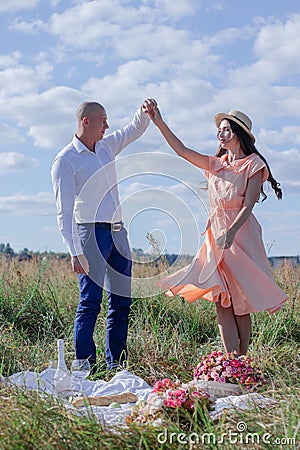 Happy couple dancing in the field. brunette in cream dress and bald man in white shirt and blue pants. love story. husband and Stock Photo