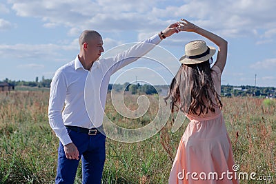 happy couple dancing in the field. brunette in cream dress and bald man in white shirt and blue pants. love story Stock Photo