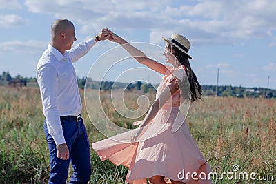 happy couple dancing in the field. brunette in cream dress and bald man in white shirt and blue pants. love story Stock Photo