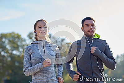 Happy couple with earphones running outdoors Stock Photo