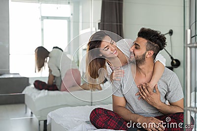 Happy Couple Embracing In Bed, Young Man And Woman Smiling Sit In Bedroom Hugging And Looking At Each Other Stock Photo