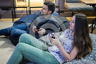 Happy couple friends playing video games with joystick sitting on Bean bag chair Stock Photo