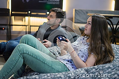 Happy couple friends playing video games with joystick sitting on Bean bag chair Stock Photo