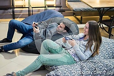 Happy couple friends playing video games with joystick sitting on Bean bag chair Stock Photo